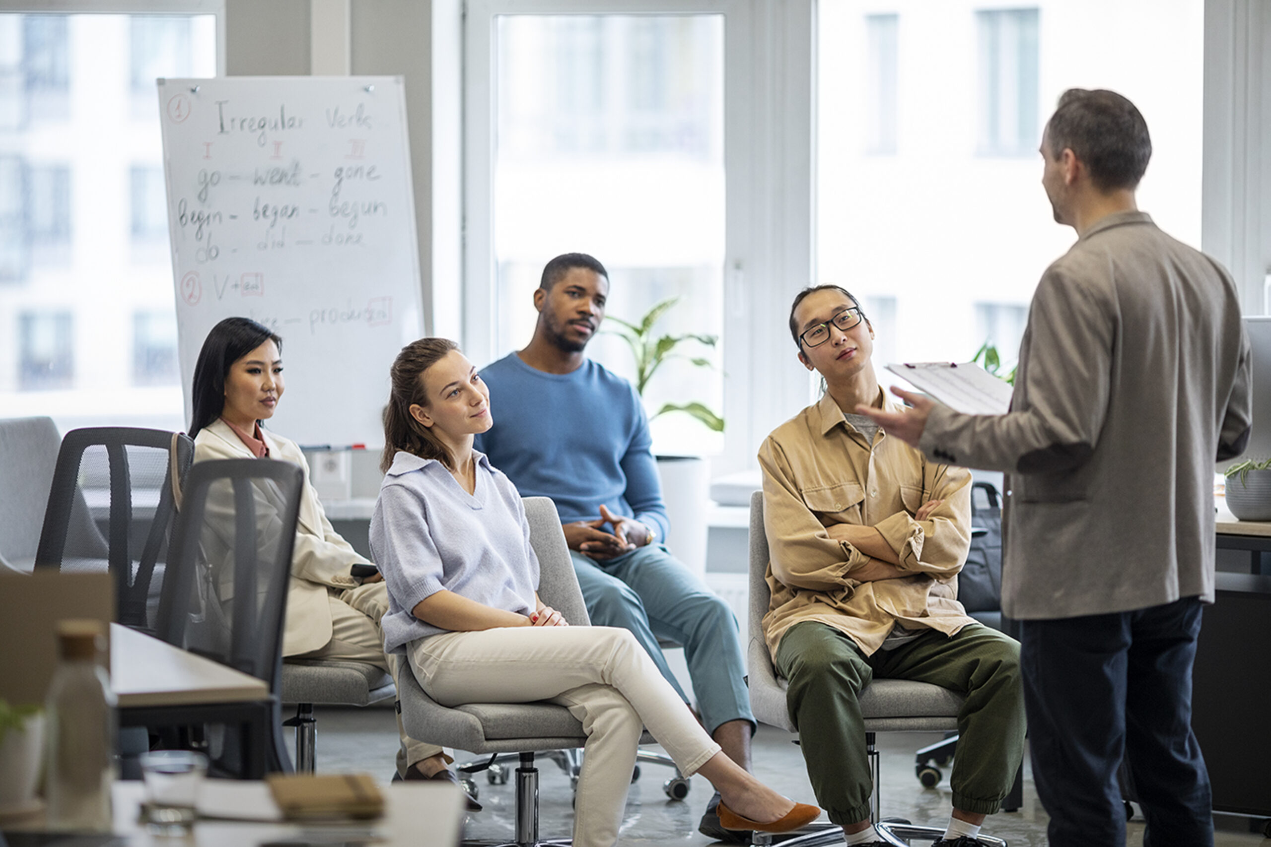 Diverse group of adults intently listening to an instructor in a bright seminar room, ideal for processes to record and monitor teacher training.