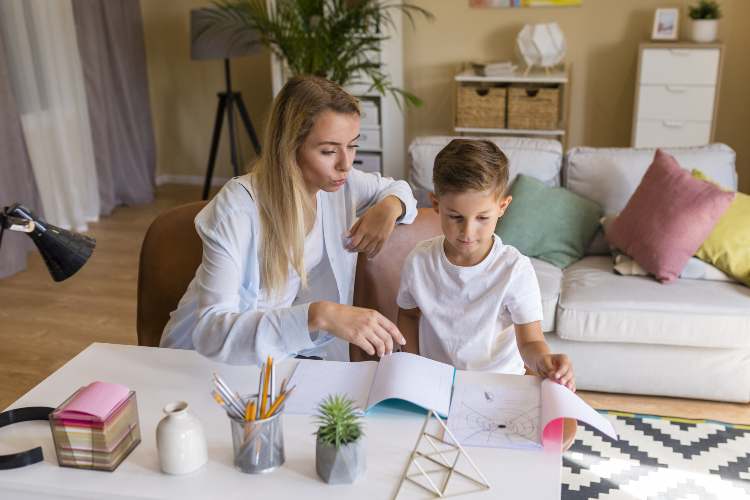 A mother and son sit at a desk reviewing a drawing in a notebook.
