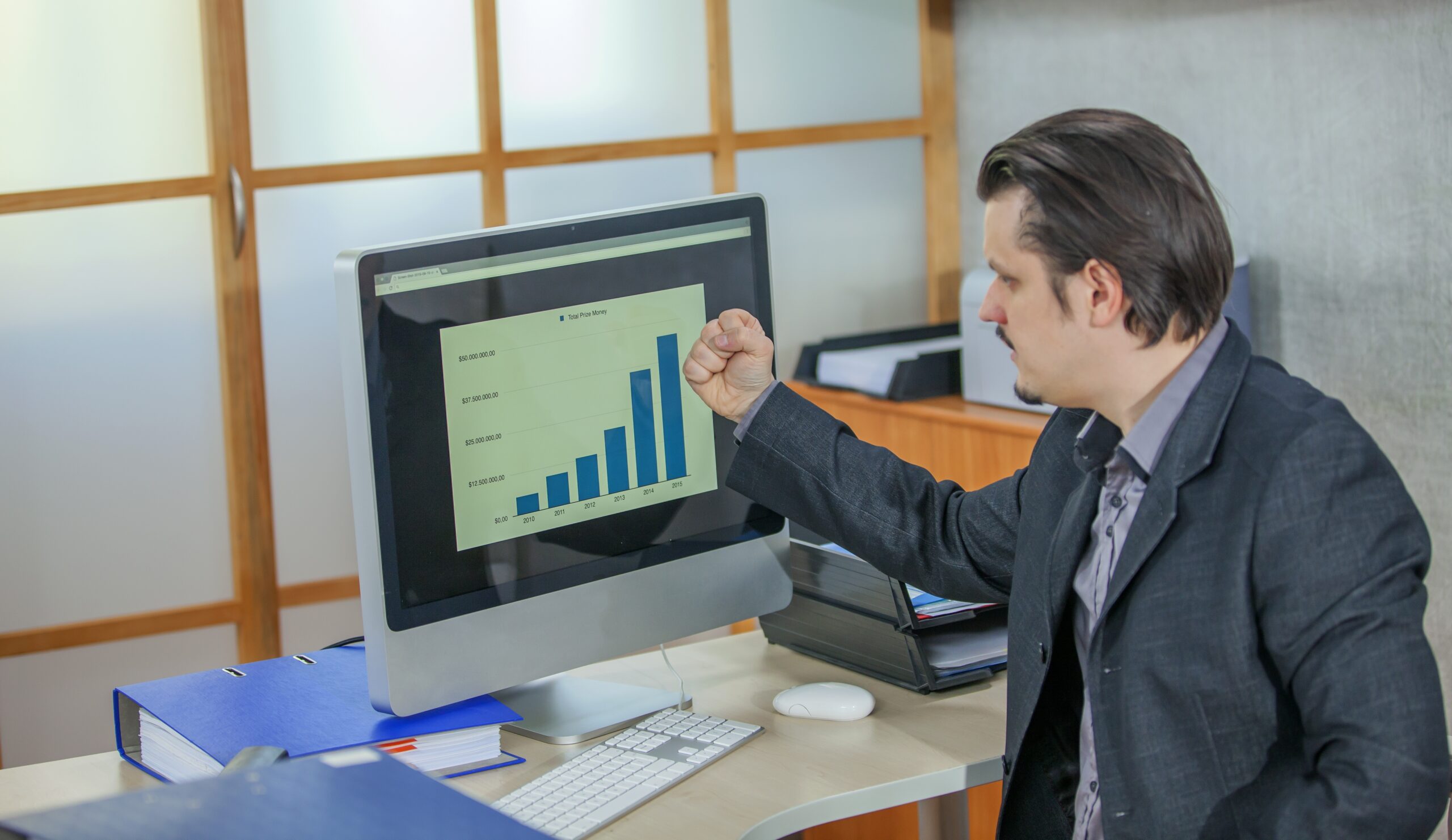 Excited man celebrating successful growth shown on a graph displayed on his computer monitor in an office.